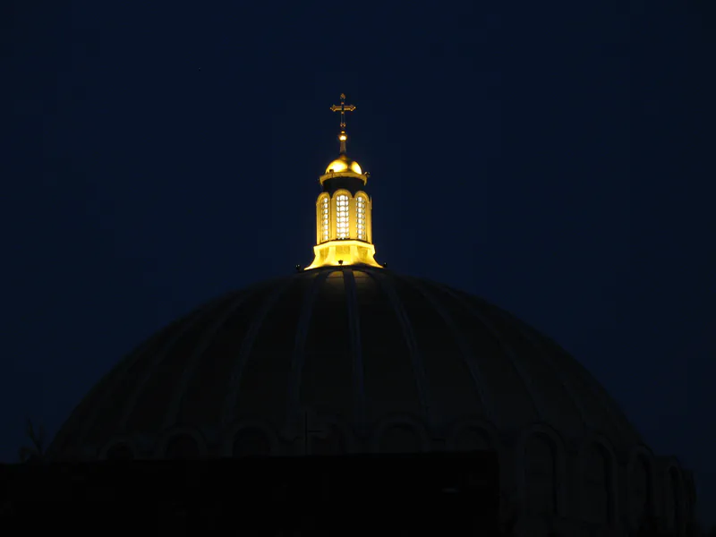 Gold-leafed lantern and cross glowing at dusk atop a church dome