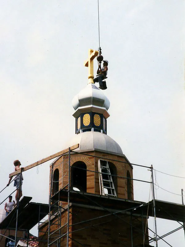 Gold cross lowered by crane onto a scaffolded onion dome