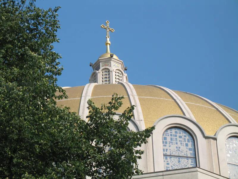 Gold-leafed church dome with gilded cross against a clear blue sky