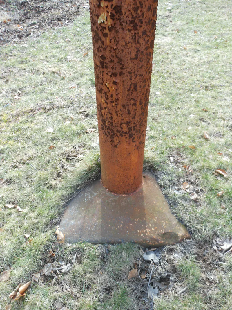 Badly corroded flagpole base at grade, flagged for repair