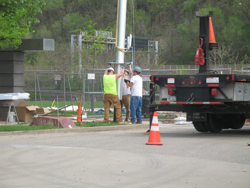 Three-man crew steadying a flagpole off the truck bed during installation