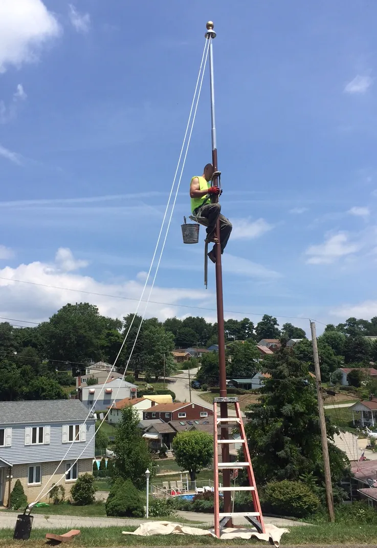 Climber refinishing a flagpole with a paint bucket hung from the belt