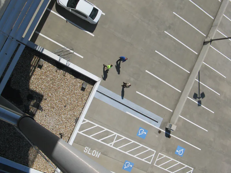 View down from a high-rise rooftop edge to a parking lot far below