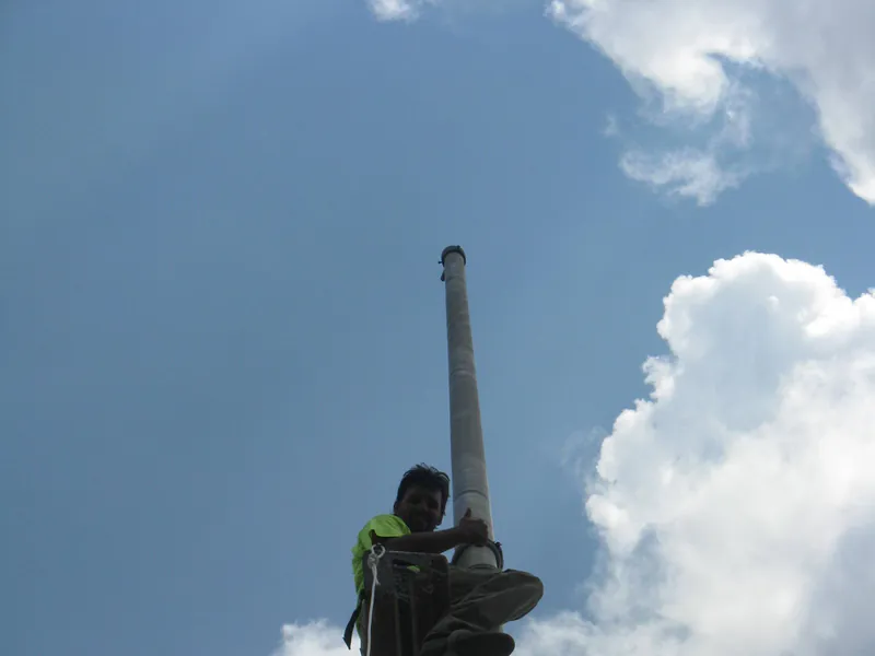 Climber near the top of a rooftop mast against a blue sky