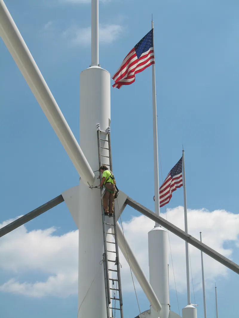 Climber on a fixed ladder at the spreaders of a white roof mast with flags flying
