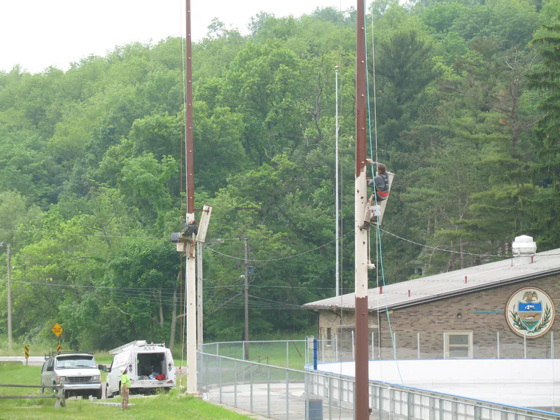Crews working platforms on two light poles at once beside a rink building