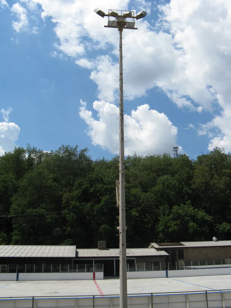 Tall light pole rising above a skating rink under a blue sky