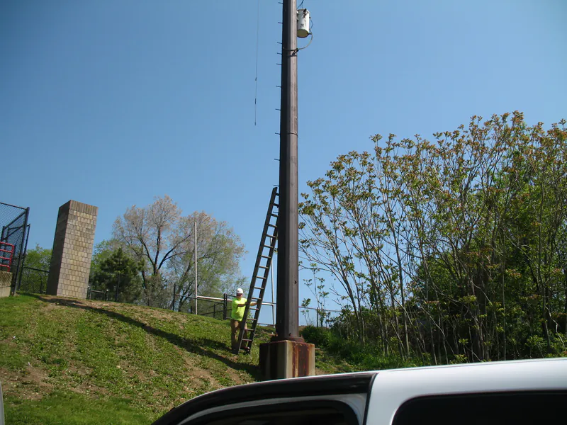 Ladder set at the base of a stadium light tower on a grass bank