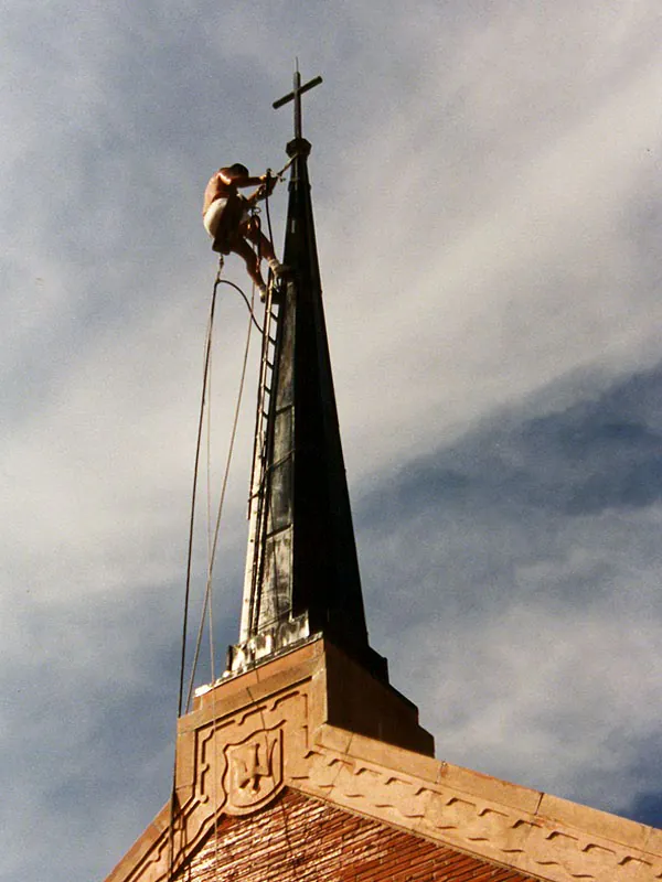 Steeplejack on a ladder lashed to a church spire working at the cross