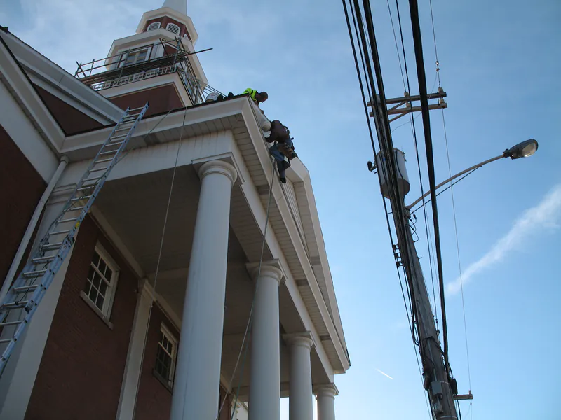 Extension ladder up a church portico to the belfry with crew on the roof